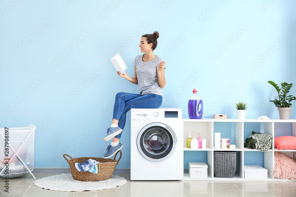 Beautiful young woman reading book while doing laundry at home