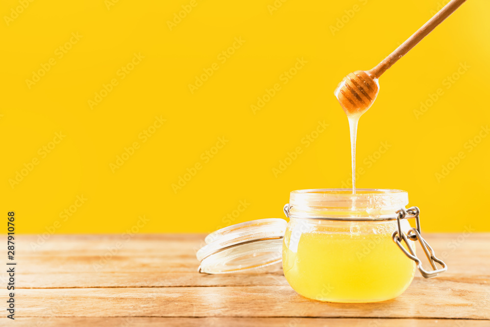 Jar and dipper with tasty honey on color background
