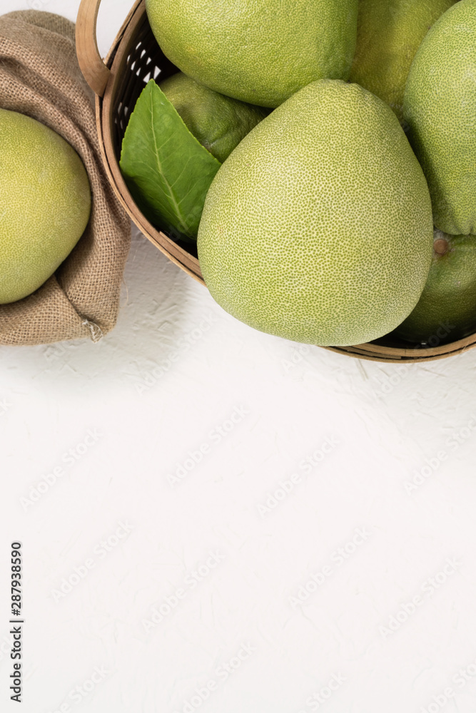 新鲜柚子，装在竹篮子里的柚子，明亮的白色背景上有绿叶。时令水果