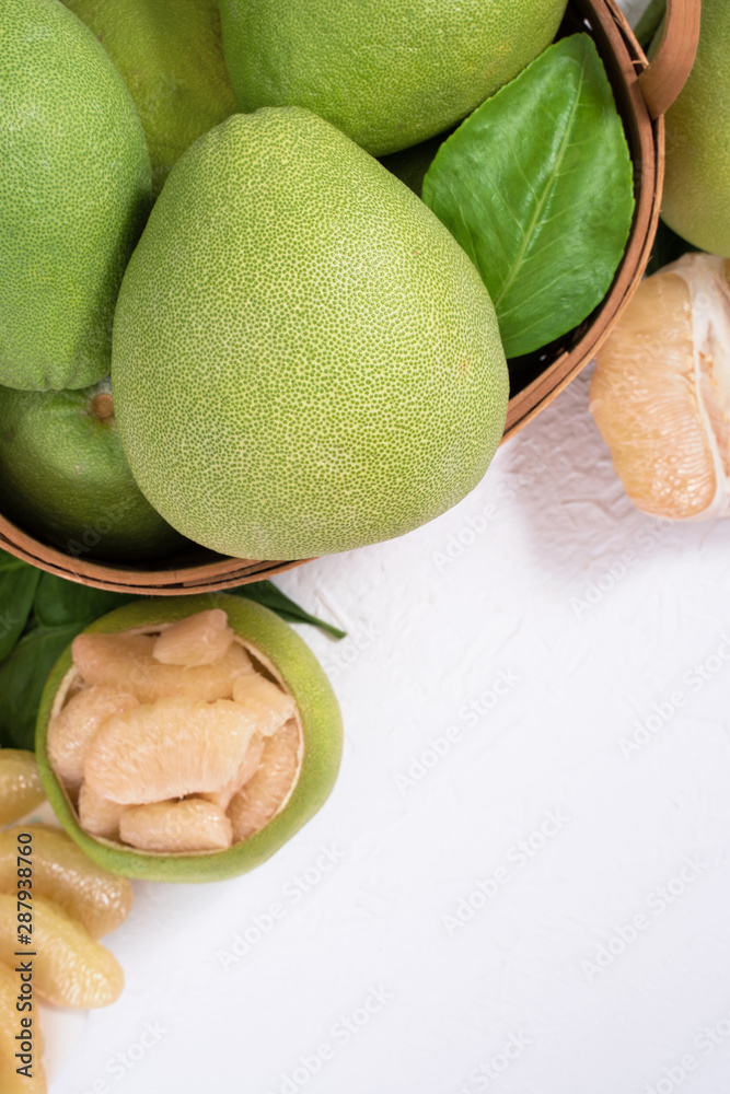 Fresh pomelo, grapefruit in bamboo basket with green leaf on bright white background. Seasonal fruit