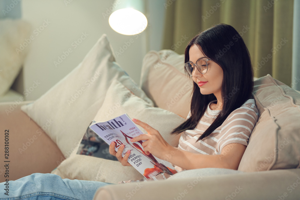 美丽的年轻女子晚上在家看杂志