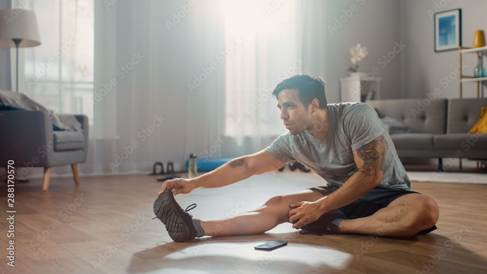 穿着T恤和短裤的强壮运动型男子在家晨练时伸展身体
