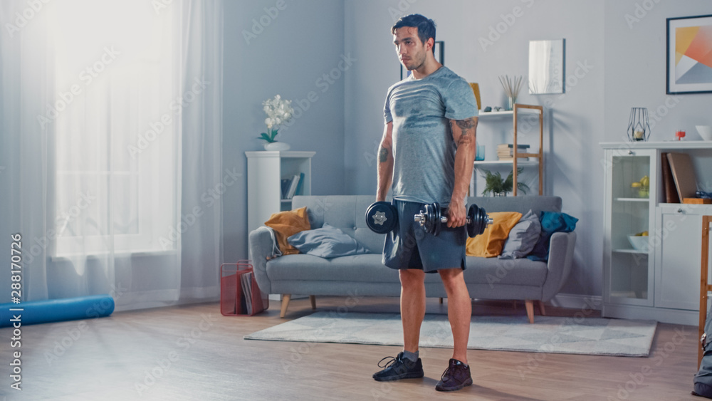 穿着T恤和短裤的肌肉运动健身男子在家里的水疗中心用哑铃锻炼