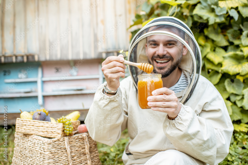 一位穿着防护服的快乐养蜂人的肖像，上面有蜂蜜产品和甜水果