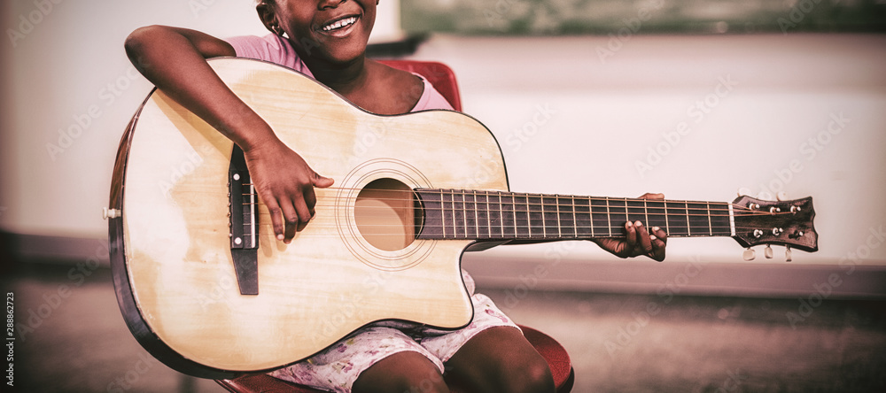 微笑的女学生在教室里弹吉他的肖像
