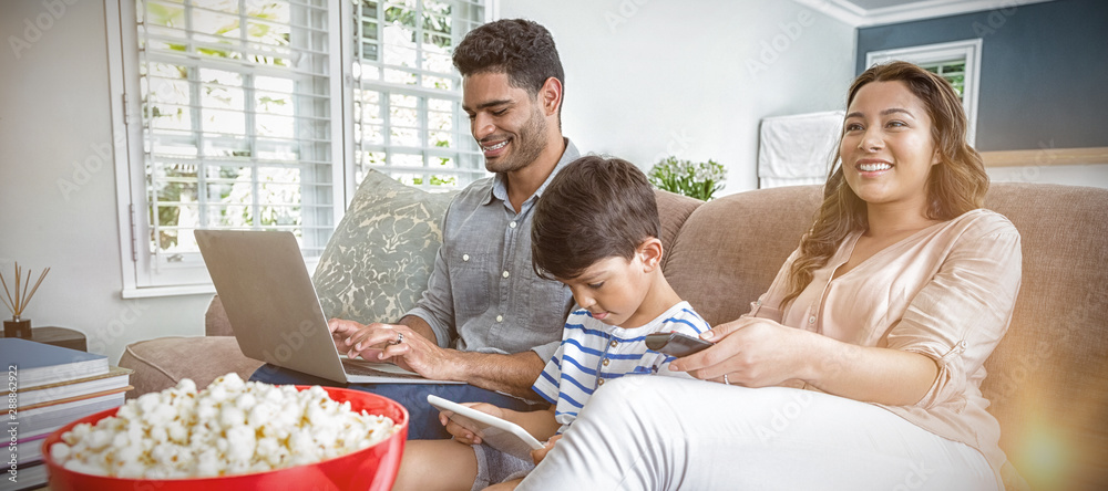 母亲在看电视，而父亲和儿子在使用笔记本电脑和数字平板电脑