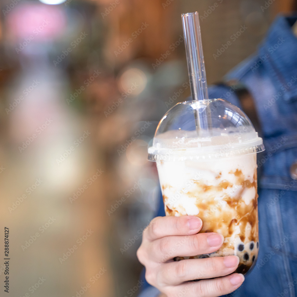 Young girl in denim jacket is drinking brown sugar flavored tapioca pearl bubble milk tea with glass