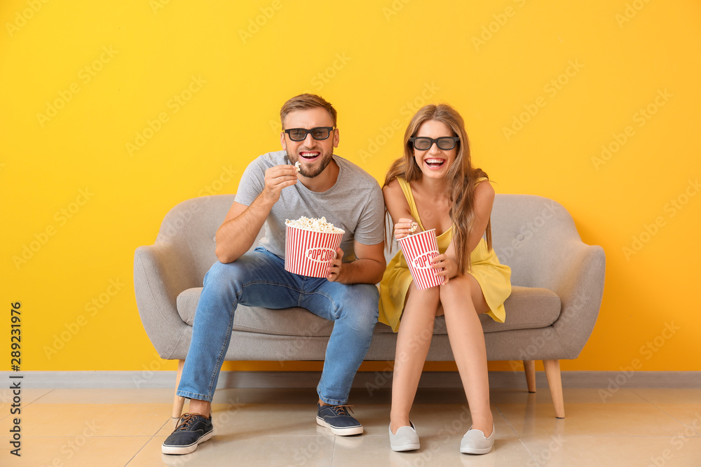 年轻夫妇拿着爆米花在靠近彩色墙的沙发上看电影