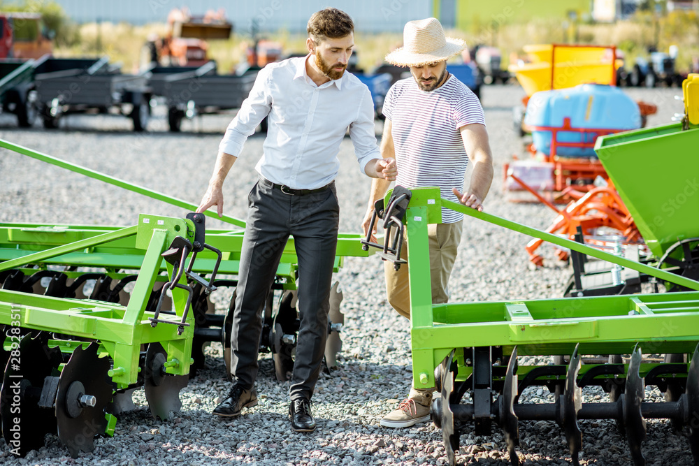 年轻的农学家和销售员或经理在商店的空地上用农业机械