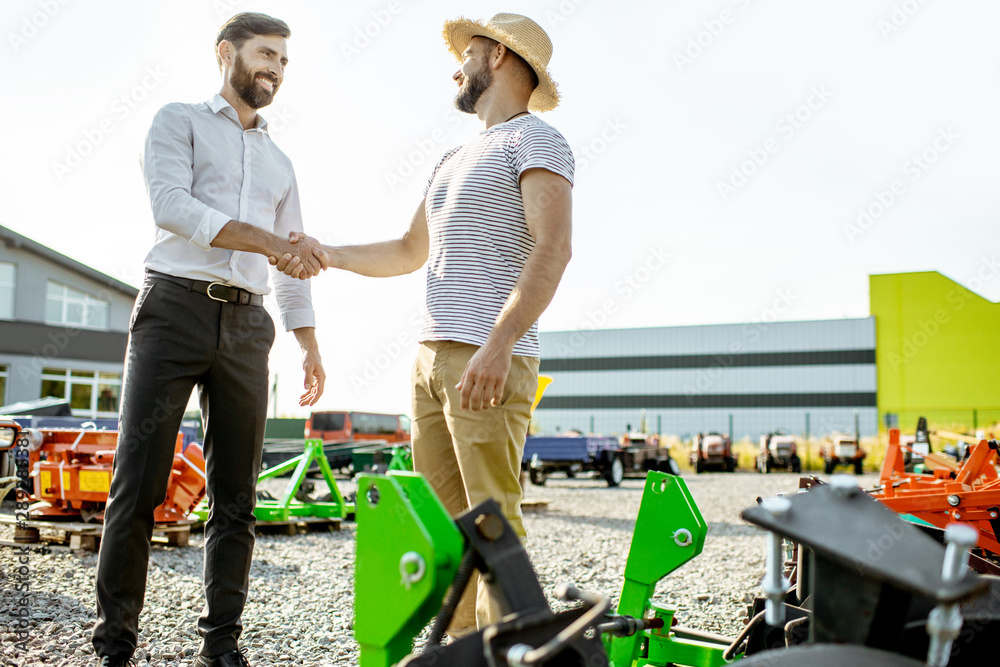 Agronomist shaking hand with salesman, having a deal about purchase a new agricultural machinery on 