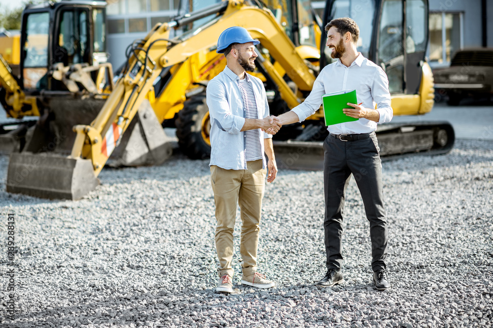 Builder choosing heavy machinery for construction with a sales consultant shaking hands on the open 