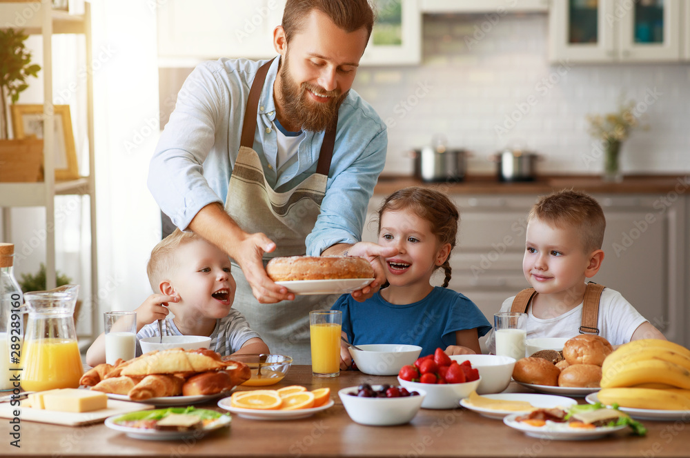 有孩子的幸福家庭父亲在厨房用早餐喂养儿子和女儿