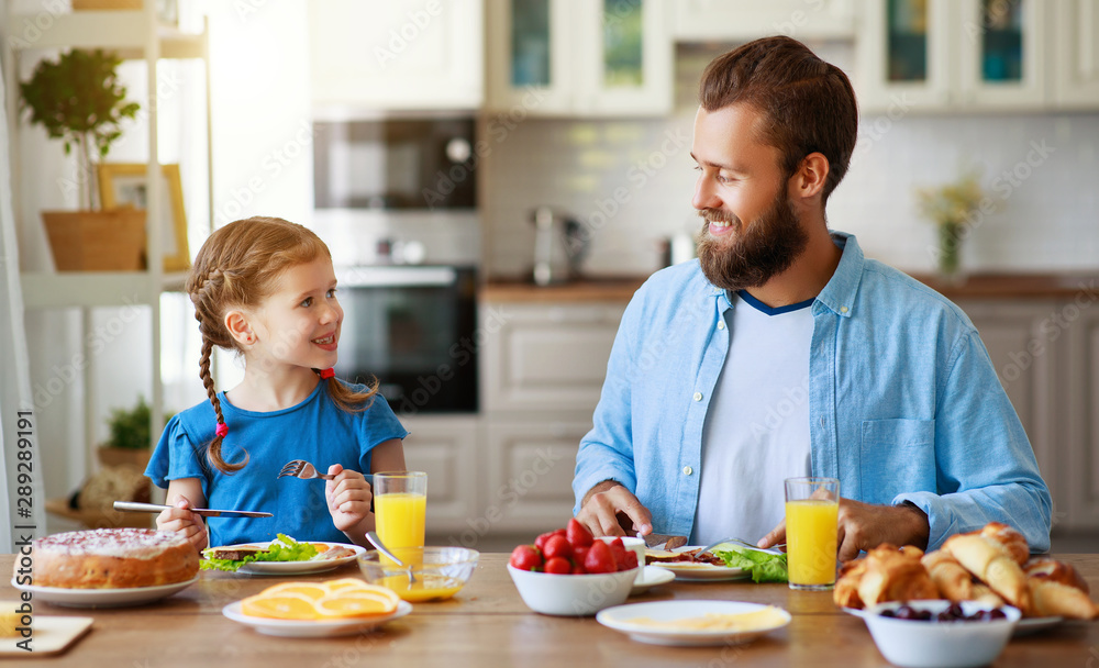 有孩子的幸福家庭父亲在厨房用早餐喂养女儿