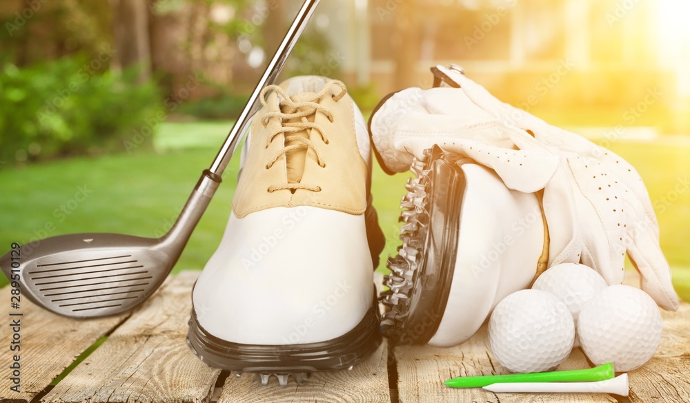 A pair of golfing shoes and a golf club on  background