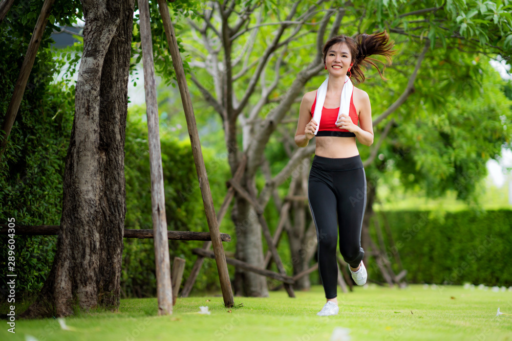 在美丽的夏日，慢跑的女人在阳光下的公园里跑步。运动健身模特亚洲人