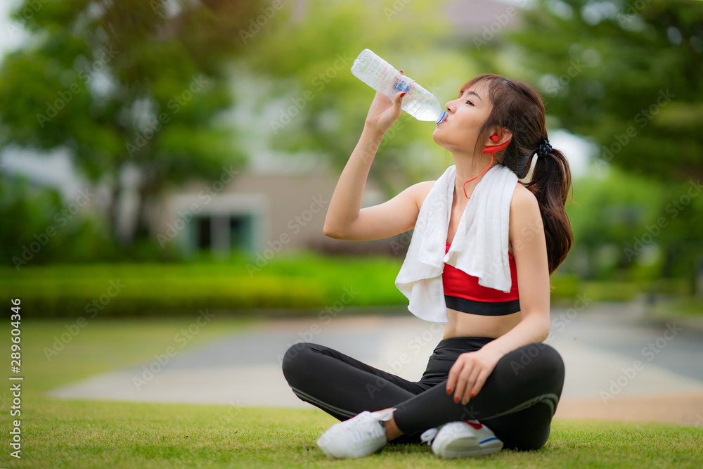 穿着红色连衣裙的亚洲迷人运动女性在慢跑或跑步后从瓶子里喝水