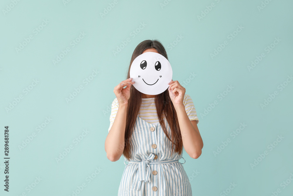 一个女人把脸藏在一张纸后面，彩色背景上画着表情符号
