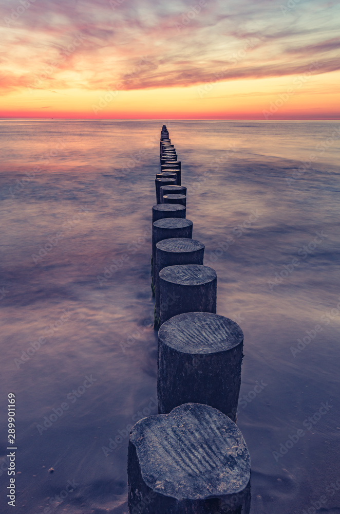 日落时的波罗的海海景，波兰，木制防波堤和波浪