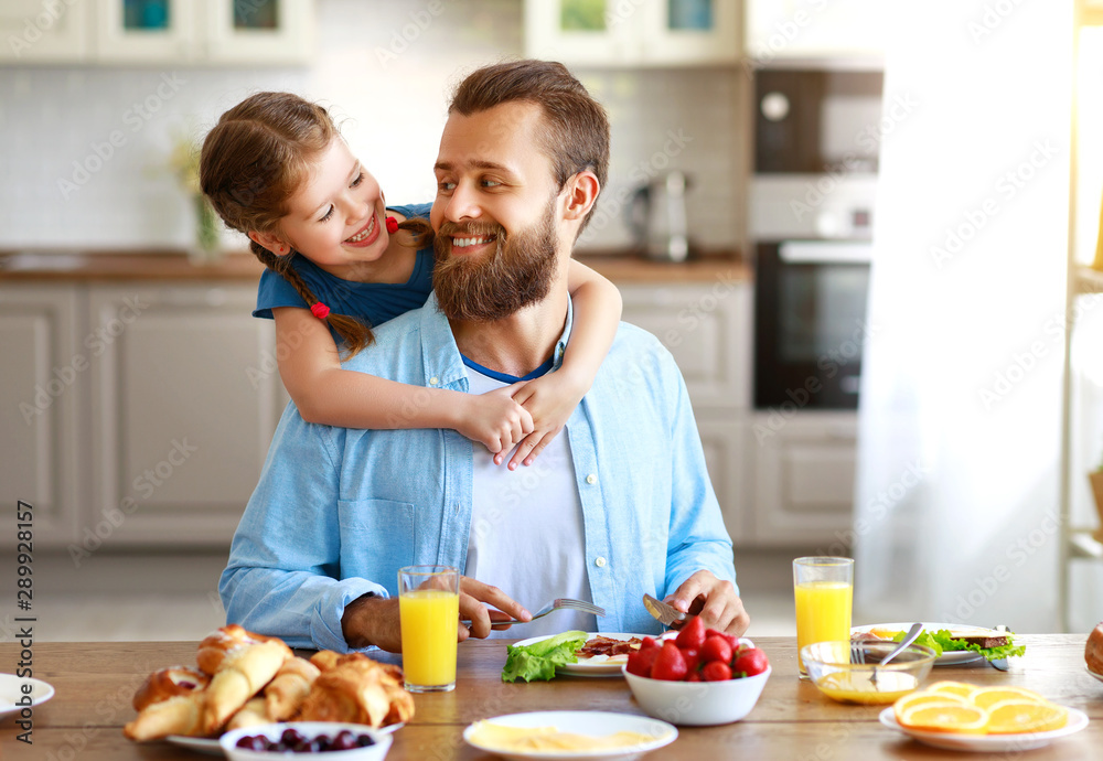幸福的家庭父亲带着孩子在厨房里用早餐喂养他的女儿。