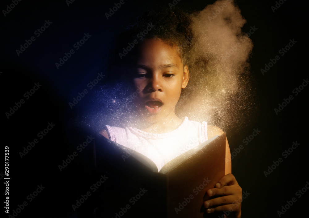 在黑暗背景下阅读魔法书的非裔美国女孩大吃一惊