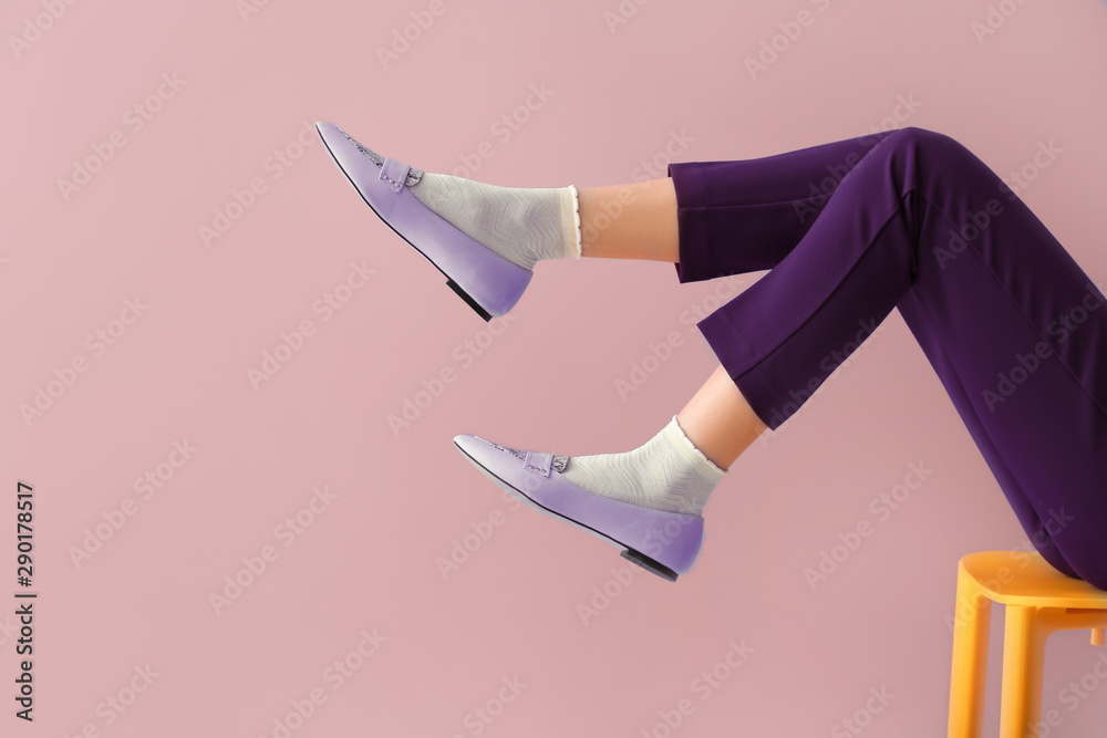 Legs of beautiful young woman sitting on chair against color background