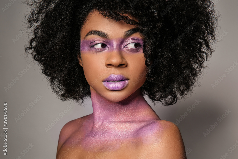 灰色背景下，身上涂着紫色油漆的非裔美国妇女