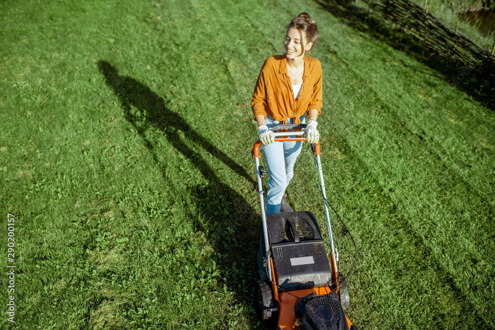 Beautiful young woman cutting grass with gasoline lawn mower, gardening on the backyard in the count