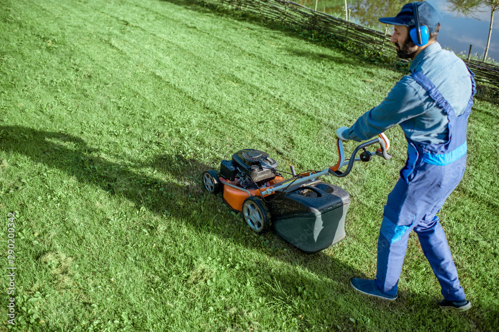 Professional gardener in protective workwear cutting grass with gasoline lawn mower on the backyard