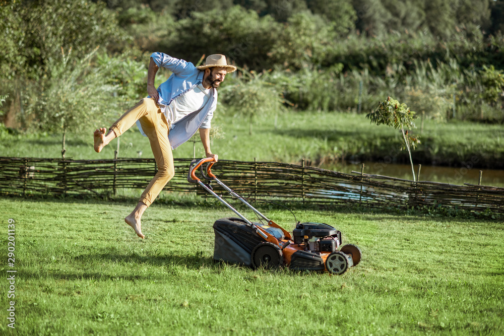 一个顽皮的男人在用汽油割草机割草时跳跃，在草坪上享受园艺过程