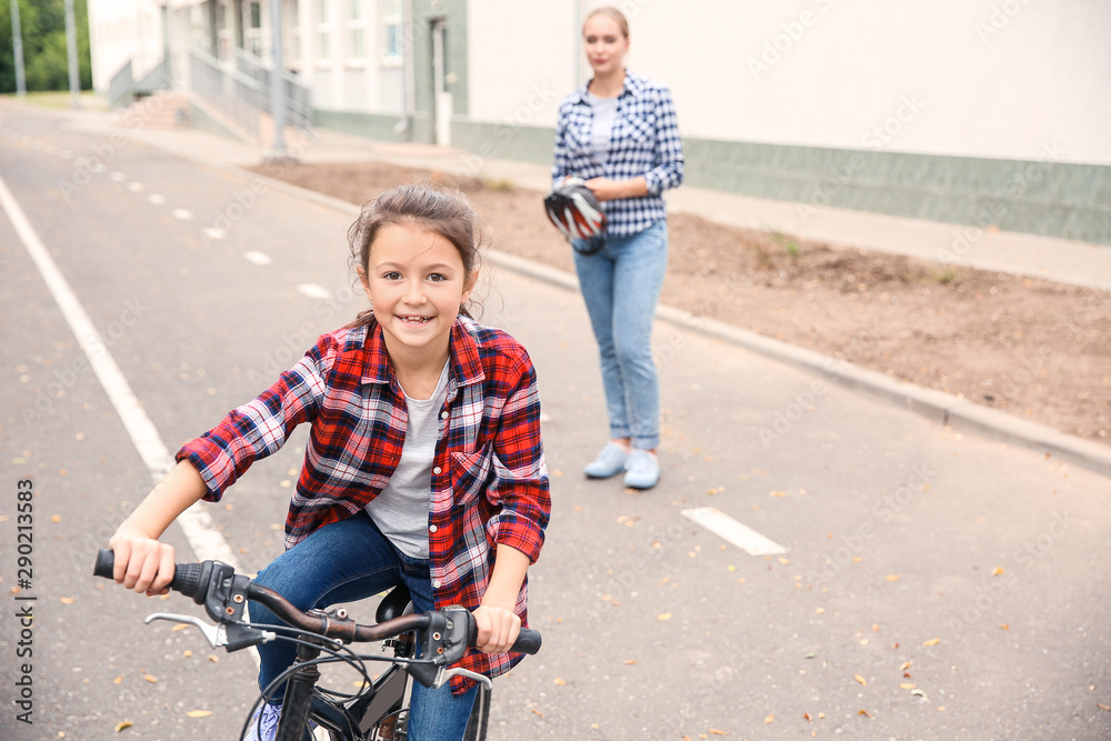 母亲在户外照看骑自行车的小女儿