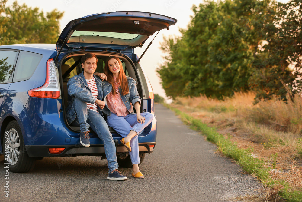 幸福的一对夫妇坐在乡下新车的后备箱里