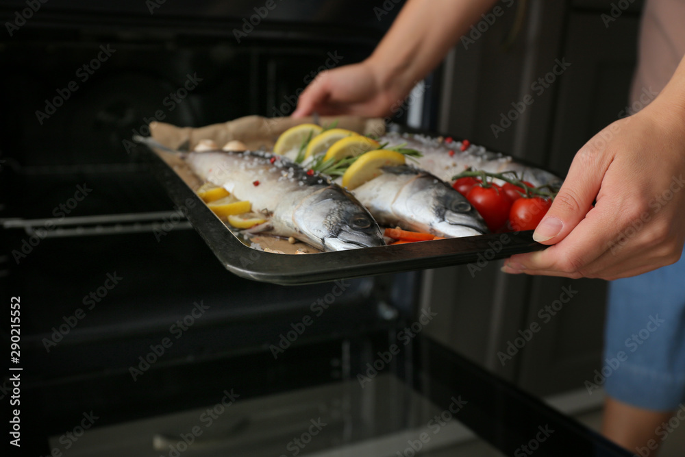 女人把盛有生鲭鱼和蔬菜的托盘放进烤箱