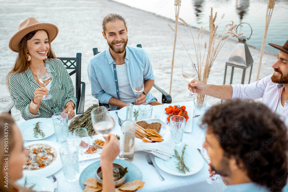 一对年轻夫妇与朋友在湖边海滩上装饰精美的桌子旁用餐