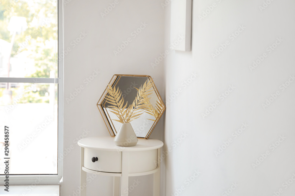 白色墙壁附近桌子上有金色热带树叶的镜子和花瓶