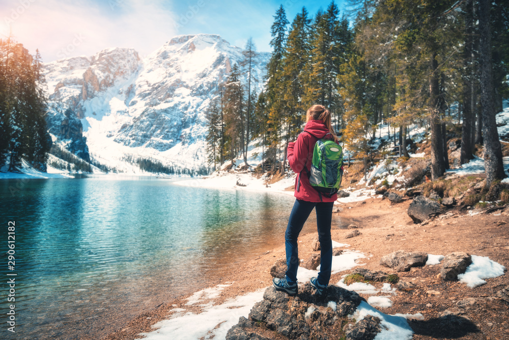 秋日阳光明媚，背着背包的年轻女子站在湖水湛蓝的湖边的石头上