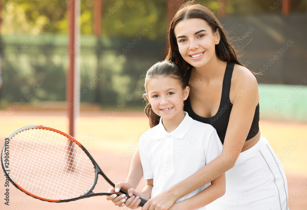 小女孩和她的妈妈在球场上打网球