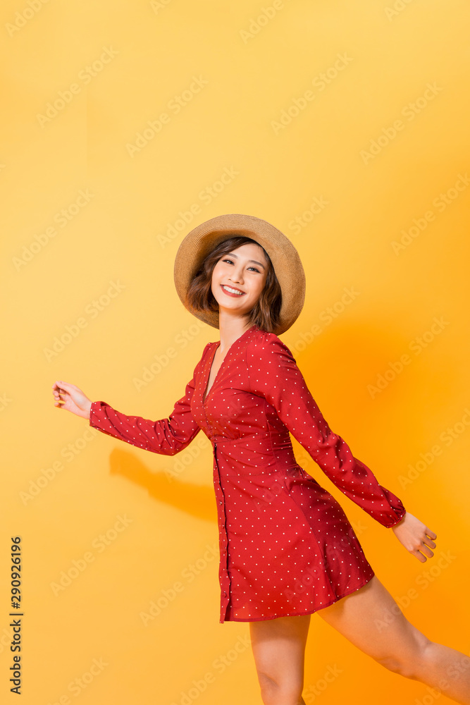 身穿红色连衣裙、戴着帽子的强大女孩在橙色背景下摆出放松姿势