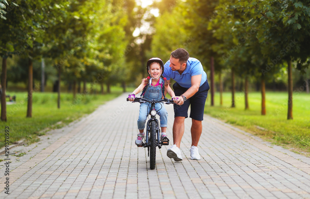 幸福的家庭父亲在公园里教孩子女儿骑自行车。