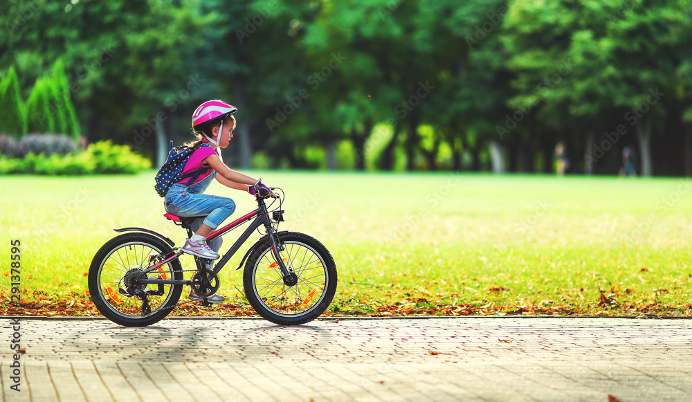 快乐快乐的小女孩在大自然的公园里骑自行车。