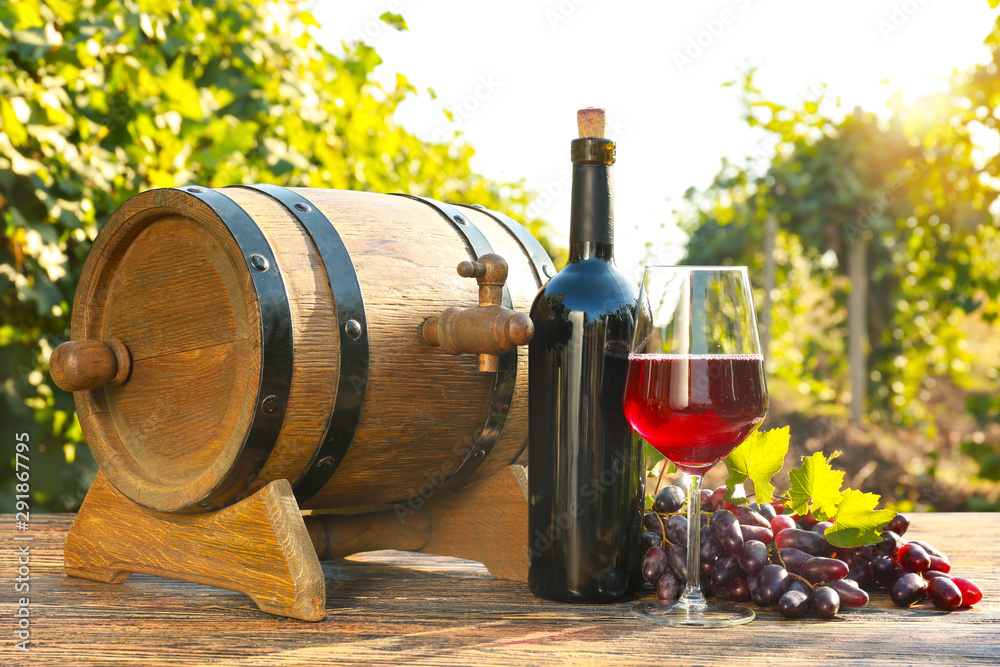 葡萄园木桌上的装有新鲜葡萄和木桶的玻璃杯和酒瓶