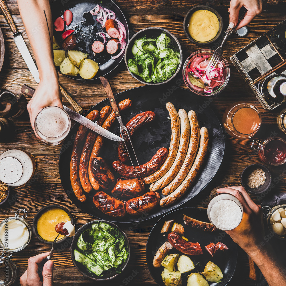 Flat-lay of Octoberfest dinner table with grilled sausages, pretzel pastry, potatoes, cucumber salad