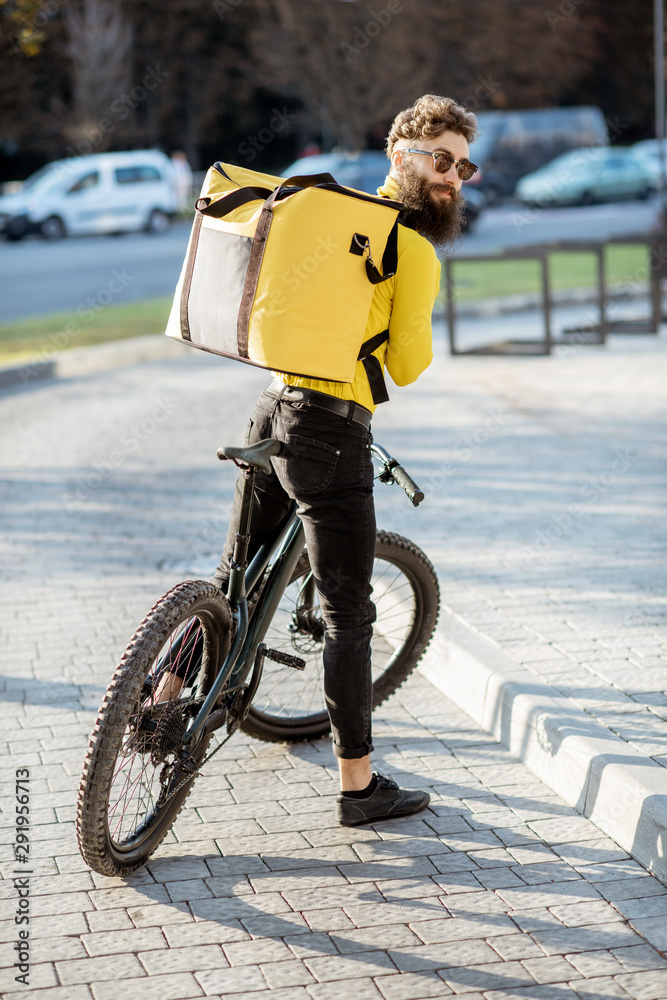 一位年轻的快递员在城市里骑着自行车，背着黄色的保温背包运送食物的肖像。