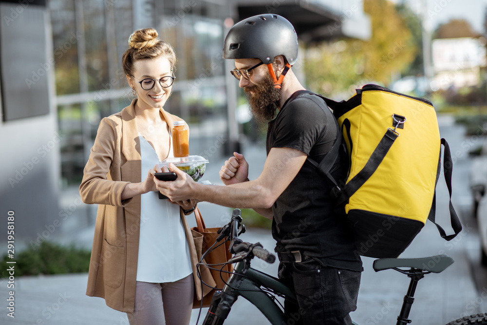 快递员用热背包骑自行车给一位年轻的商务女性送新鲜午餐。Takea