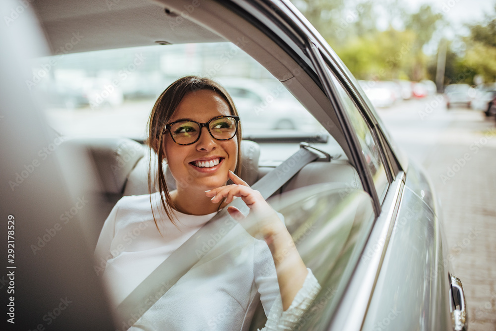 一位坐在汽车后座上向窗外望去的快乐年轻女子的画像。