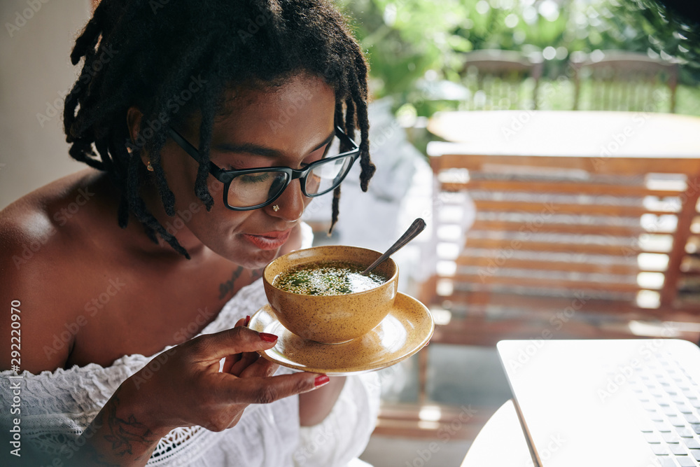 非洲年轻女子，留着漂亮的发型，戴着眼镜，手里拿着盛着汤的碗，她是甲状腺肿