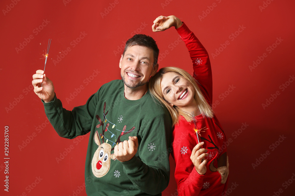 Happy couple with Christmas sparklers on color background