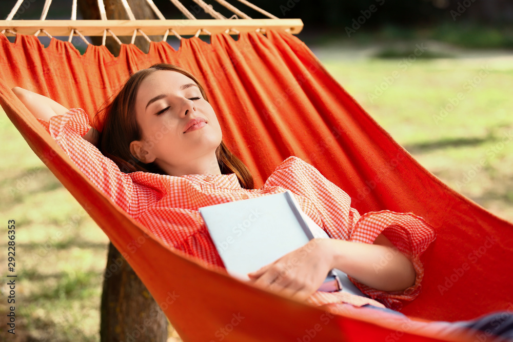 美丽的年轻女子在户外吊床上看书