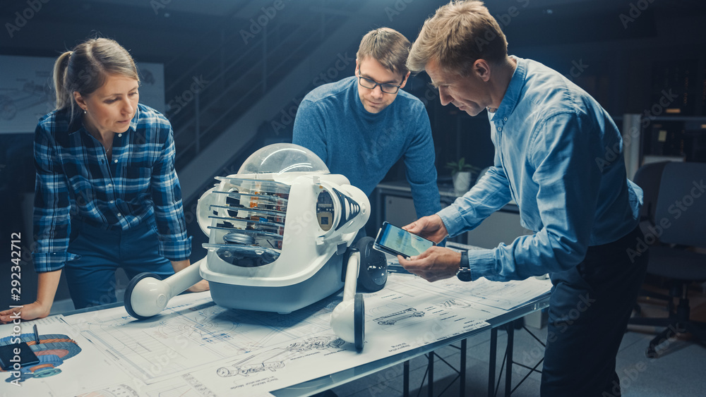 机器人工程设施三位技术工程师在轮式机器人原型上交谈和工作。