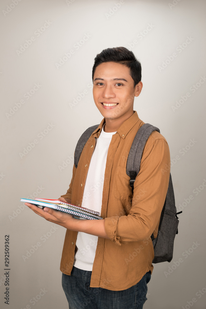 自信英俊的亚洲学生拿着书对着镜头微笑