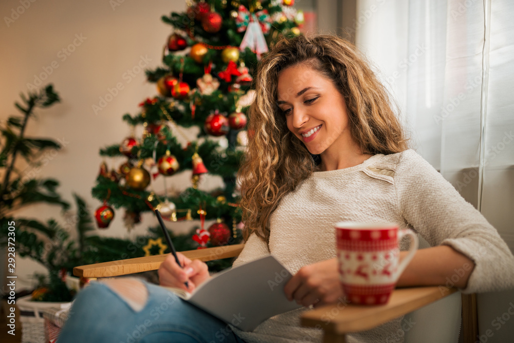 一个在家里用铅笔和笔记本写字的女人的肖像。圣诞节、冬天、节日和人们